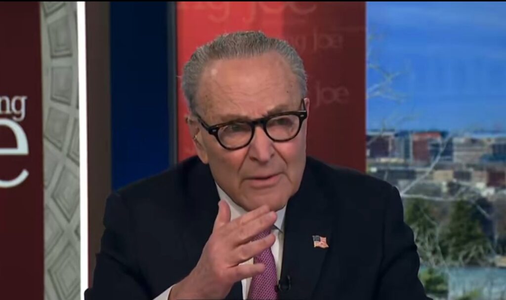 Chuck Schumer sitting with hand up