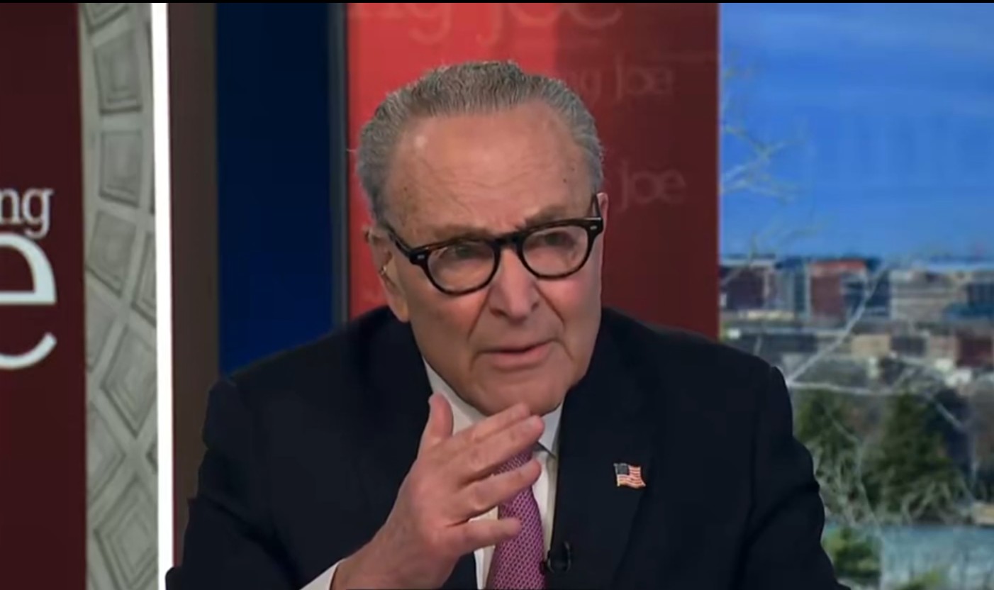 Chuck Schumer sitting with hand up